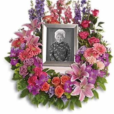 Colorful wreath of pink lilies, roses, and mixed blooms surrounding a framed portrait.