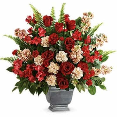 Tall arrangement of red roses and peach carnations in a gray urn-style vase