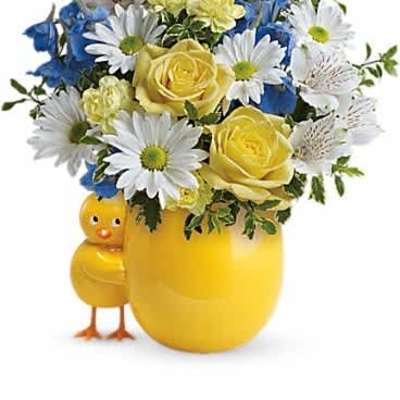 Yellow and white flower arrangement in a yellow vase with an attached chick figurine