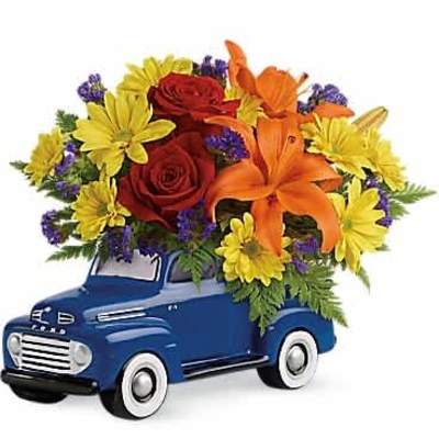 Mixed bouquet of orange lilies, red roses, and yellow flowers arranged in a blue ceramic pickup truck container