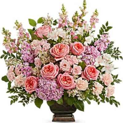 Large pink and lavender bouquet of roses, hydrangeas, carnations, and snapdragons in a dark pedestal vase.