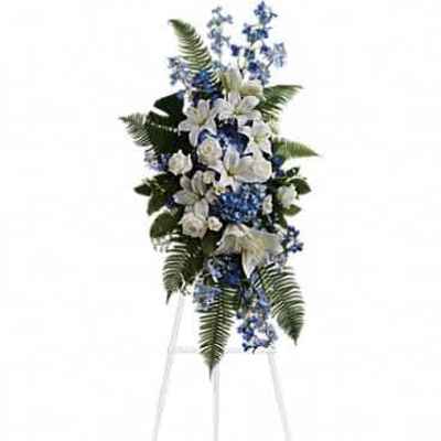 Tall standing spray of white lilies and roses with blue flowers on a white easel