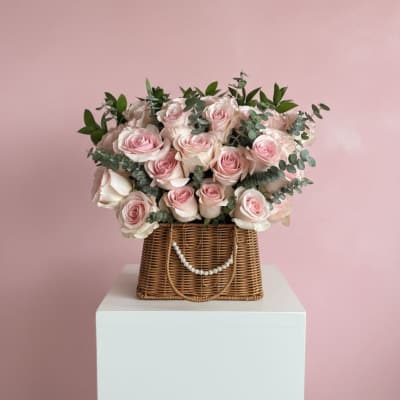 Pink roses arranged in a wicker basket with greenery