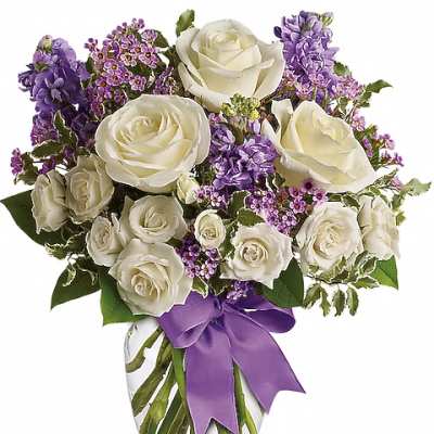 White roses and purple flowers arranged in a glass vase with a purple ribbon