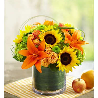 Orange lilies and sunflowers in a glass vase with green accents