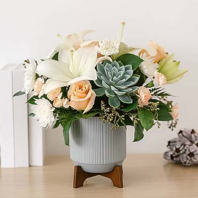 Arrangement of white lilies, peach roses, and a blue-green succulent in a ribbed vase