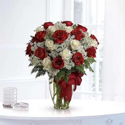 Red and white roses arranged in a clear glass vase with a red ribbon