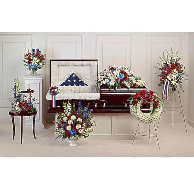 Funeral casket surrounded by red, white, and blue floral sprays