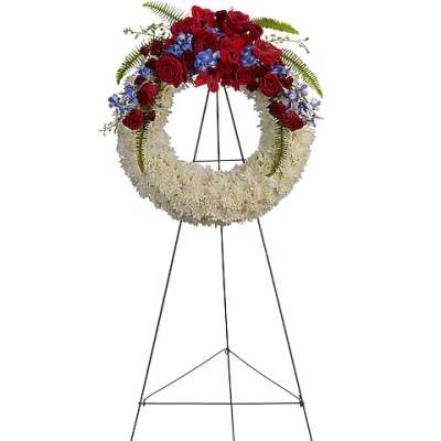 Standing funeral wreath with red roses, blue flowers, and white blooms on an easel