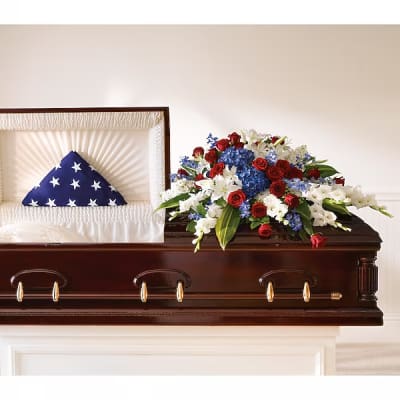 Casket with a patriotic flag display and red, white, and blue floral spray