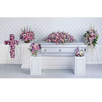Floral funeral display with pink and purple arrangements around a white casket