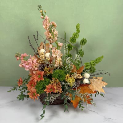 Autumn floral arrangement in a wicker basket with peach, orange, and green blooms