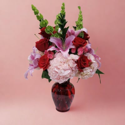 Bouquet of red roses, pink lilies, and pale hydrangeas in a red glass vase