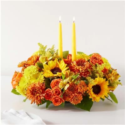 Yellow and orange floral centerpiece with two lit taper candles