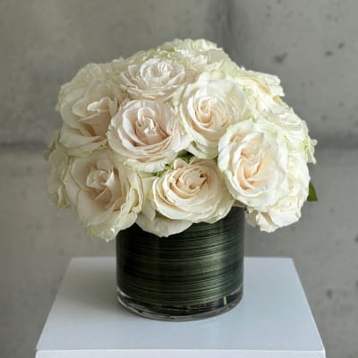 White roses arranged in a dark glass vase on a white pedestal