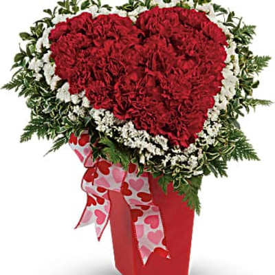 Heart-shaped red carnation arrangement in a red vase with a heart ribbon