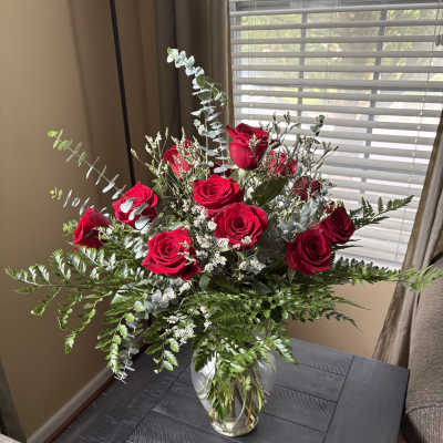 Red roses arranged in a clear glass vase with airy greenery