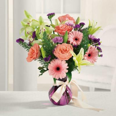 Mixed bouquet of pink and coral flowers in a purple glass vase with a ribbon
