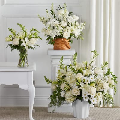 Three white floral arrangements in vases and a basket on pedestals