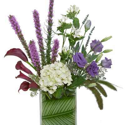 Tall mixed bouquet with purple and white flowers in a glass vase