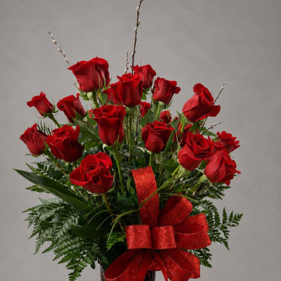 Red roses arranged in a tall red vase with a glittery red bow
