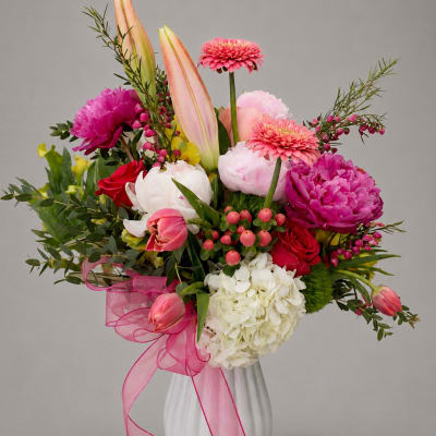 Pink and white mixed flower arrangement in a white vase with a pink ribbon