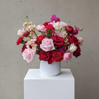 Mixed pink and red flowers arranged in a white vase