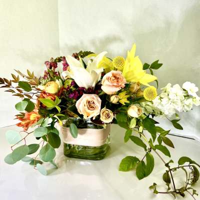 Mixed bouquet in a square glass vase with white lilies and yellow blooms