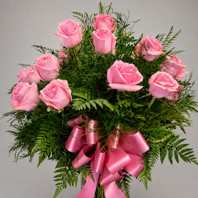 Pink roses arranged in a clear glass vase with a pink ribbon