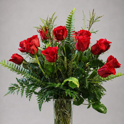 Red roses arranged in a clear glass vase with greenery