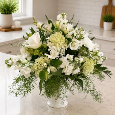 White floral arrangement in a white vase with trailing greenery