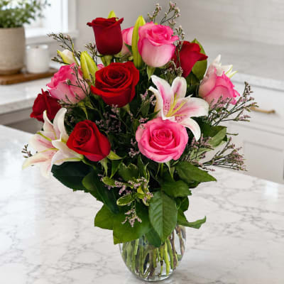 Bouquet of red and pink roses with white lilies in a clear glass vase