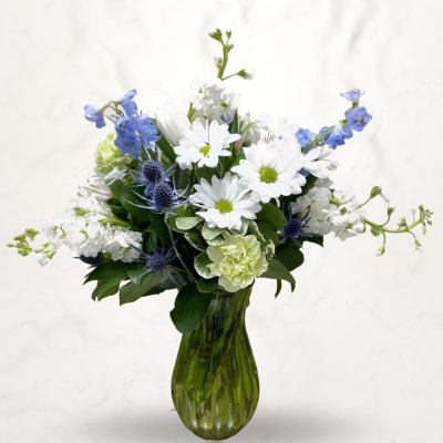 White daisies and blue flowers arranged in a green glass vase