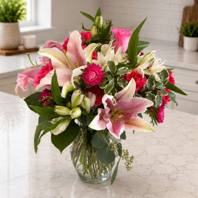 Pink lilies and mixed flowers arranged in a clear glass vase