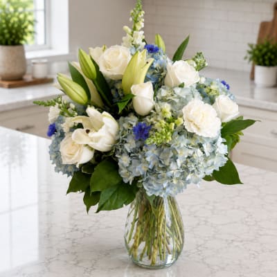 White roses, lilies, and blue hydrangeas in a clear glass vase