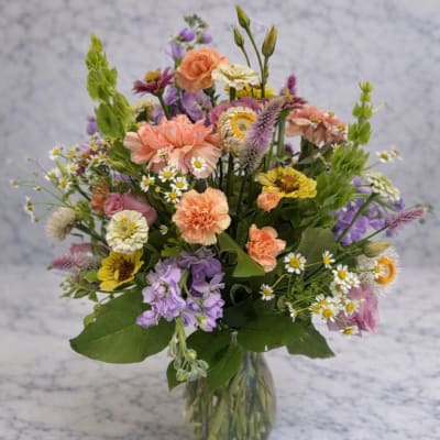 Mixed bouquet of peach, purple, white, and yellow flowers in a clear vase