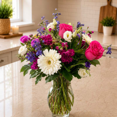 Mixed bouquet of pink roses, white gerbera daisies, and purple flowers in a glass vase