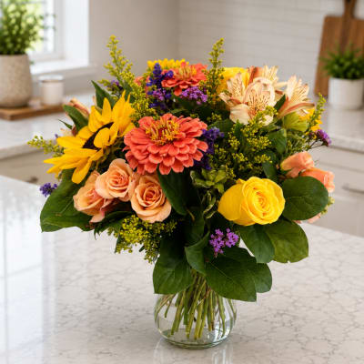 Mixed bouquet of yellow, peach, and purple flowers in a clear glass vase
