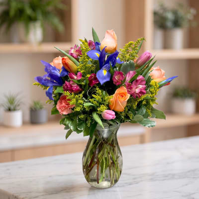 Mixed bouquet of roses, tulips, irises, and alstroemeria in a glass vase