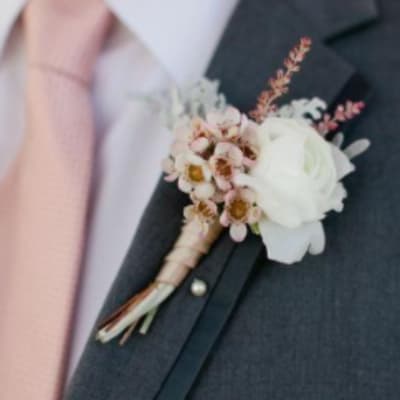 White and blush boutonniere pinned to a dark suit jacket