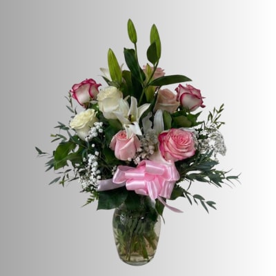 Pink and white rose bouquet with lilies in a glass vase and pink ribbon