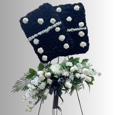 White floral standing spray on an easel with a black floral tribute board above it