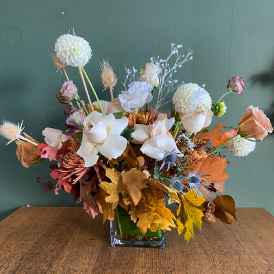 Mixed floral arrangement in a square glass vase with autumn leaves