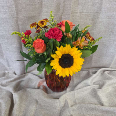 Mixed bouquet with a sunflower, roses, carnations, and alstroemeria in a red glass vase