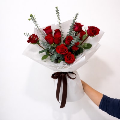 Bouquet of red roses wrapped in white paper with a dark ribbon