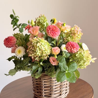 Mixed floral arrangement in a woven basket with pink, peach, white, and green blooms
