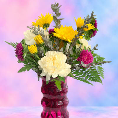 Mixed bouquet of yellow, white, and magenta flowers in a pink vase