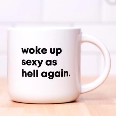 White mug with bold black text reading "woke up sexy as hell again."