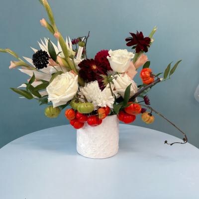 White and burgundy floral arrangement in a white vase with orange berries