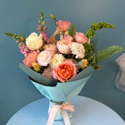 Pastel bouquet of roses, tulips, and mixed blooms wrapped in blue paper